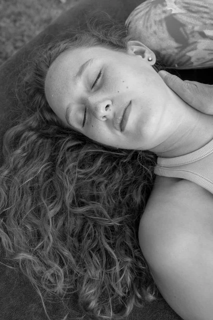 Portrait noir et blanc d'une jeune femme recevant un soin énergétique dans le cou, l'air détendu