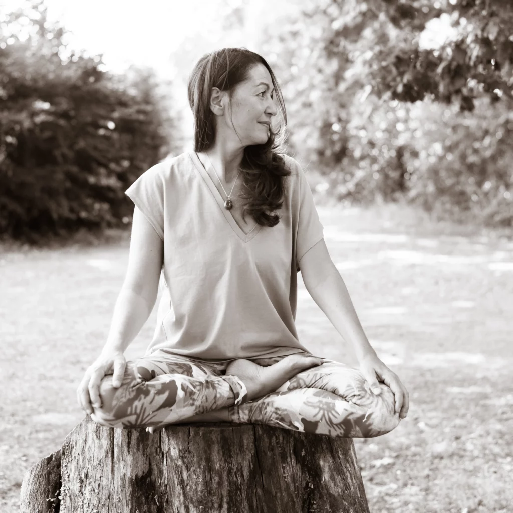 Portrait format carré en sépia de Patrizia Buscemi, assise dans une posture de yoga sur la souche d'un arbre, le regard tourné vers la droite de l'image
